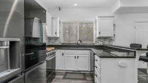 Kitchen with white cabinets, stainless steel fridge, a sink, a peninsula, and gas range oven