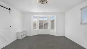 Spare room with dark carpet, a barn door, and baseboards