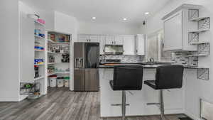 Kitchen with stainless steel refrigerator with ice dispenser, open shelves, dark countertops, and white cabinetry