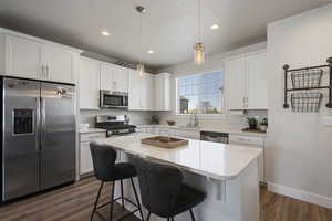 Kitchen with dark wood-style flooring, a center island, a sink, light countertops, and stainless steel appliances