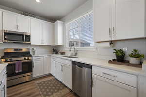 Kitchen featuring dark wood-style floors, light countertops, white cabinets, a sink, and appliances with stainless steel finishes
