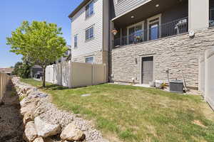 Back of property featuring a yard, fence, stone siding, and cooling unit