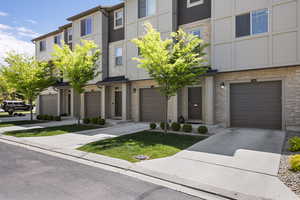 Townhome / multi-family property featuring an attached garage, driveway, and stone siding