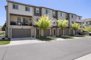 Townhome / multi-family property featuring a garage, a residential view, driveway, and stone siding