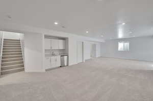 Basement with stairs, light carpet, indoor wet bar, baseboards, and a sink