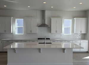 Kitchen with wall chimney range hood, tasteful backsplash, a kitchen bar, and light wood-type flooring