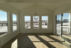 Unfurnished sunroom featuring plenty of natural light, wood finished floors, a chandelier, and vaulted ceiling