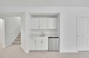 Kitchen featuring baseboards, dishwashing machine, light colored carpet, light countertops, and white cabinetry