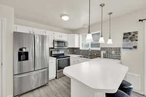 Kitchen with a breakfast bar, a sink, light countertops, stainless steel appliances, and decorative backsplash