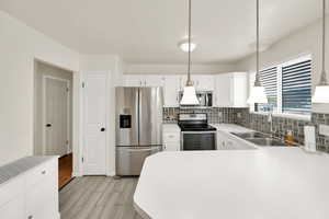 Kitchen with light countertops, tasteful backsplash, a sink, light wood finished floors, and appliances with stainless steel finishes