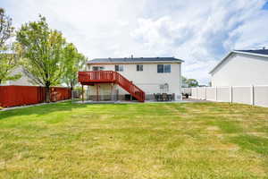 Back of property with stairs, a wooden deck, a fenced backyard, a patio, and a yard