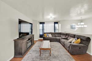 Living room featuring an inviting light fixture, baseboards, a textured ceiling, and wood finished floors