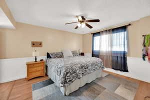 Bedroom with a ceiling fan, wainscoting, and light wood finished floors