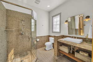 Full bathroom featuring visible vents, tile walls, a shower stall, a wainscoted wall, and toilet