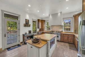 Kitchen with decorative backsplash, appliances with stainless steel finishes, a sink, light wood finished floors, and extractor fan