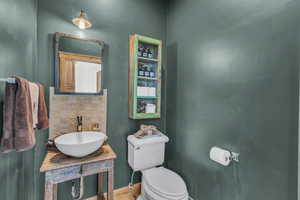 Half bathroom featuring a sink, toilet, baseboards, decorative backsplash, and wood finished floors