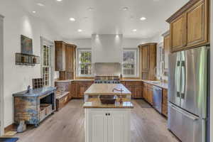 Kitchen featuring stainless steel appliances, brown cabinets, a kitchen island, light stone counters, and recessed lighting