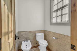 Half bath featuring wainscoting, toilet, tile walls, tile patterned floors, and a bidet