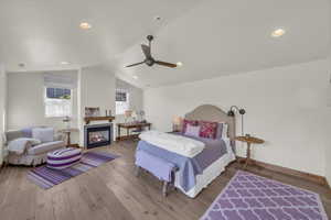 Bedroom with a glass covered fireplace, wood finished floors, lofted ceiling, baseboards, and ceiling fan