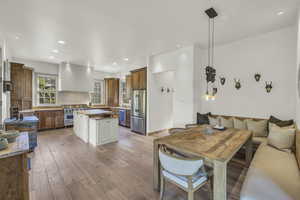 Kitchen featuring wall chimney range hood, brown cabinetry, appliances with stainless steel finishes, a center island, and light wood finished floors