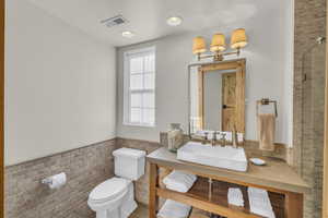 Bathroom featuring visible vents, tile walls, a wainscoted wall, vanity, and toilet
