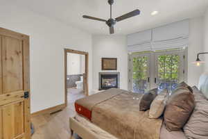 Bedroom with visible vents, access to exterior, light wood-type flooring, a glass covered fireplace, and recessed lighting