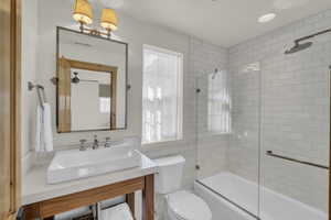 Full bath with visible vents, tile walls, bath / shower combo with glass door, vanity, and toilet
