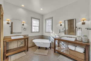 Full bath featuring a sink, wainscoting, tile walls, and a soaking tub