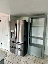 Kitchen featuring stainless steel fridge, a textured ceiling, and light tile patterned floors