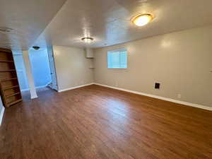 Basement featuring baseboards, built in features, a textured ceiling, and dark wood-style floors