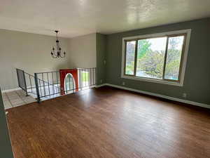 Unfurnished living room with baseboards, a textured ceiling, wood finished floors, and a chandelier