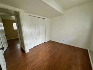 Unfurnished bedroom with baseboards, a closet, and dark wood-style floors