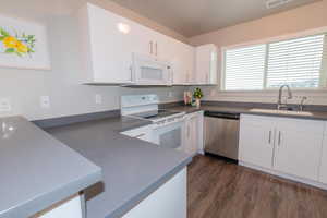 Kitchen with white appliances, white cabinets, a sink, and dark wood-type flooring