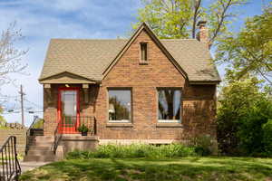 View of front of home featuring a shingled roof, a chimney, a front lawn, and brick siding
