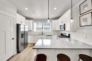 Kitchen with decorative backsplash, appliances with stainless steel finishes, a sink, a peninsula, and recessed lighting