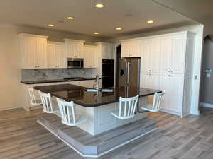 Kitchen featuring white cabinetry, a center island with sink, tasteful backsplash, a breakfast bar area, and crown molding