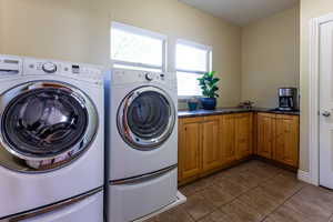 Laundry area with cabinet space, dark tile patterned floors, and washer and clothes dryer