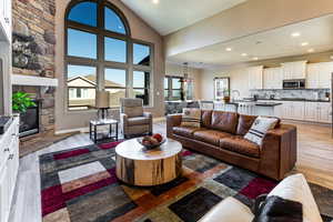 Living area featuring a stone fireplace, light wood-type flooring, lofted ceiling, ornamental molding, and recessed lighting