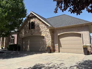 View of front of home featuring a shingled roof, stone siding, a garage, stucco siding, and concrete driveway
