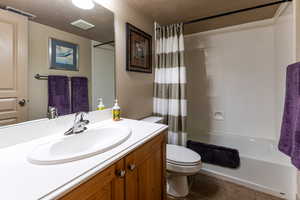 Bathroom with toilet, visible vents, shower / bathtub combination with curtain, and vanity