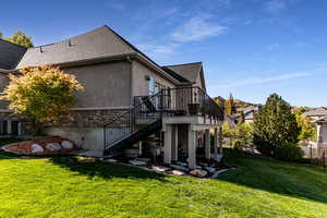 Rear view of property with fence, a shingled roof, stucco siding, stairway, and a lawn
