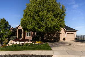 View of property hidden behind natural elements featuring an attached garage, fence, stone siding, and concrete driveway