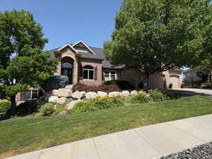 View of front facade with driveway, stone siding, a front lawn, brick siding, and a garage