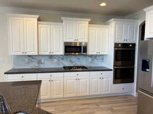 Kitchen with tasteful backsplash, appliances with stainless steel finishes, crown molding, dark stone counters, and white cabinetry