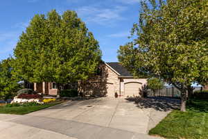 View of property hidden behind natural elements with fence, stone siding, a garage, stucco siding, and driveway