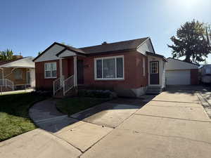 View of front facade featuring brick siding, a garage, a front lawn, and an outbuilding