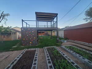 Back of house featuring a wooden deck, fence, a vegetable garden, a playground, and a lawn