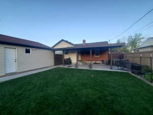 Rear view of house featuring fence, a chimney, a yard, and a patio area
