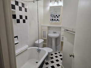 Full bathroom featuring a sink, a tub, toilet, and tile walls