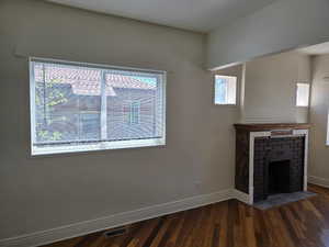 Unfurnished living room featuring a brick fireplace, baseboards, visible vents, and wood finished floors